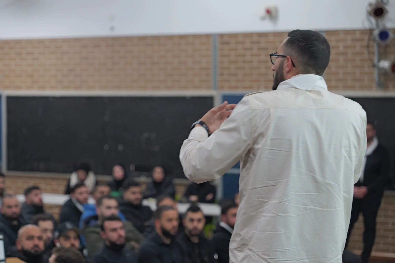 A leader speaks to a room of adults at an evening information session.