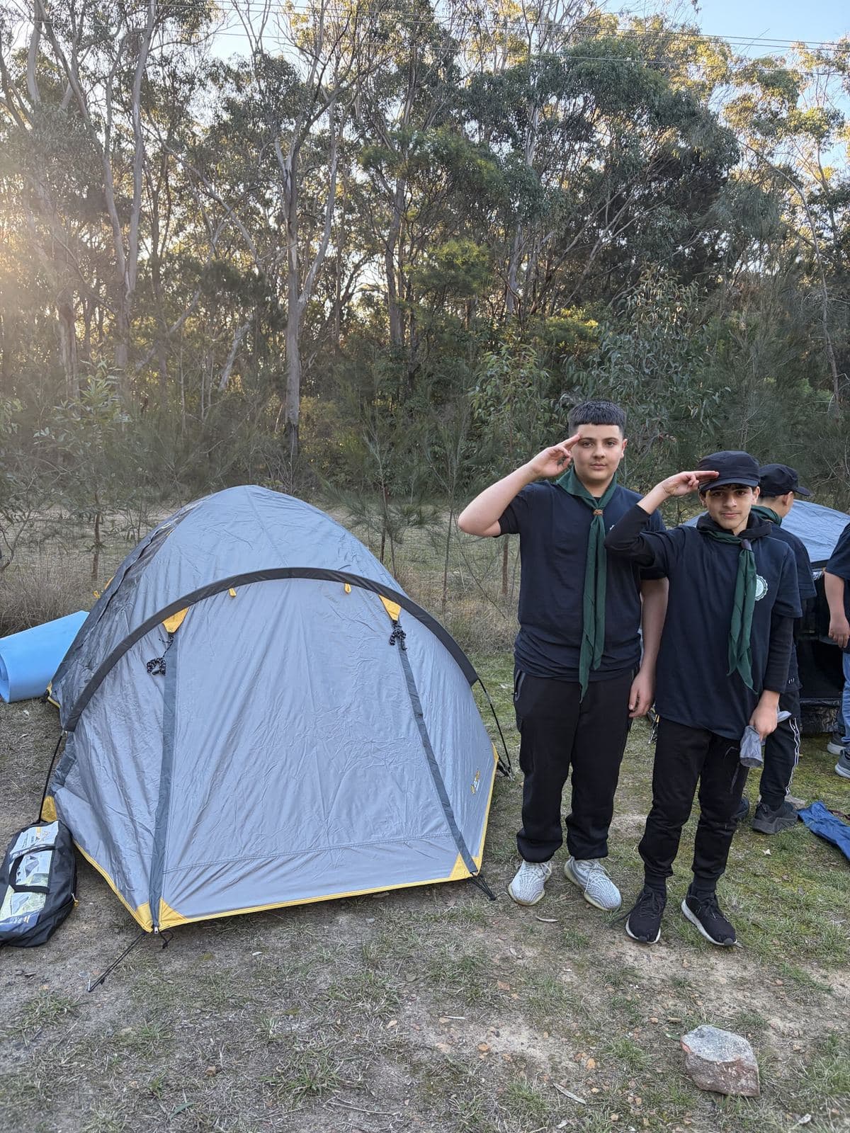 Two campers saluting beside their tent